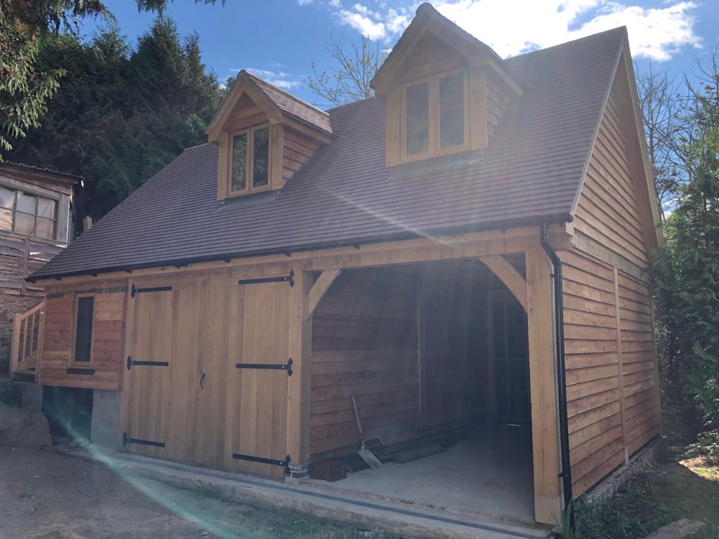 Oak framed garage with dormers above. One bays is enclosed to be used as a workshop.