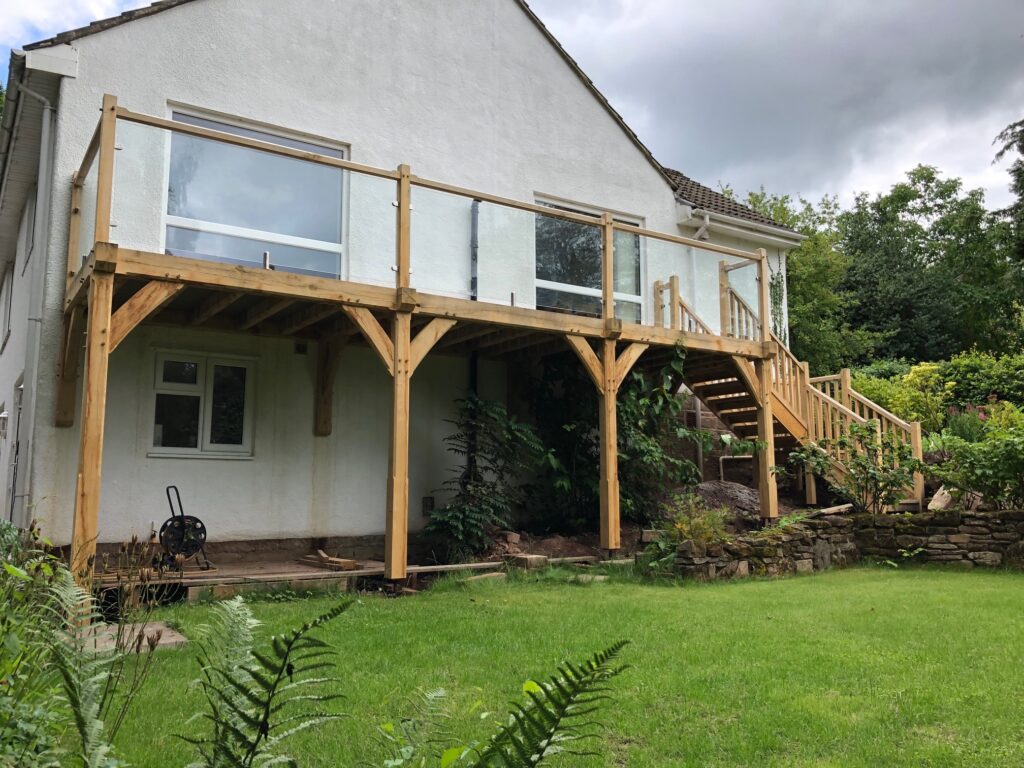 Oak framed balcony with oak posts and rails and a glass balustrade.