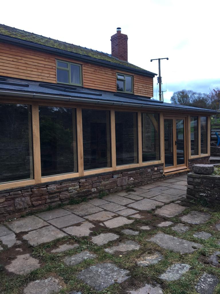 Oak Framed lean too extension, sat on a stone wall.