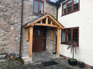 An open oak porch with two half posts bolted to the house wall and the two front post sat on stones