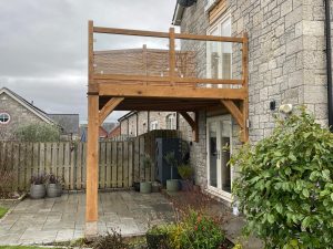 An oak framed balcony with glass balustrade fitted between oak posts and rails.